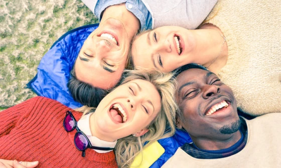 Group of young adults lying down on the grass laughing together